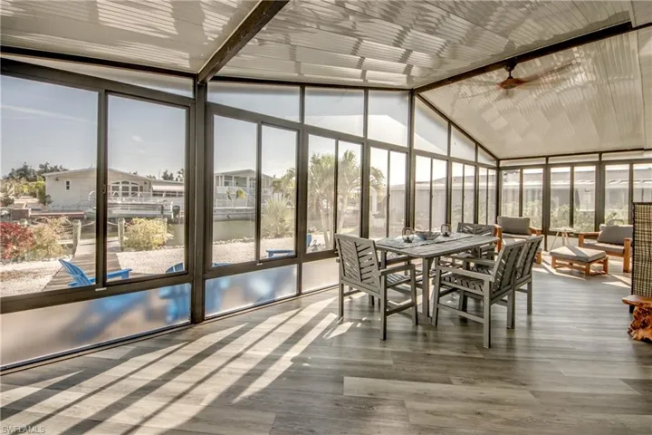 Sunroom / solarium with a ceiling fan, outdoor dining space, a wall of windows, vaulted ceiling, and wood finished floors
