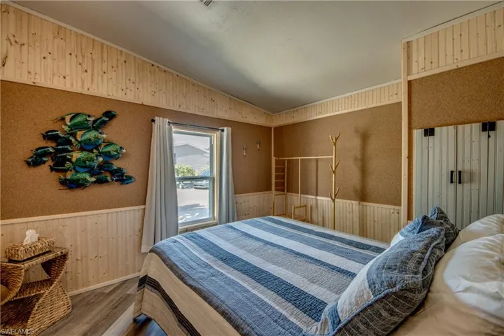 Bedroom with wainscoting, wood walls, vaulted ceiling, wood finished floors, and wallpapered walls