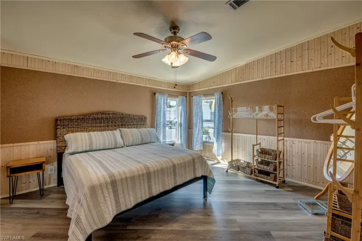 Bedroom featuring a wainscoted wall, wood walls, lofted ceiling, wood finished floors, and a ceiling fan