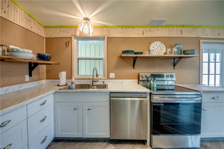 Kitchen with open shelves, appliances with stainless steel finishes, white cabinetry, and light wood-style flooring