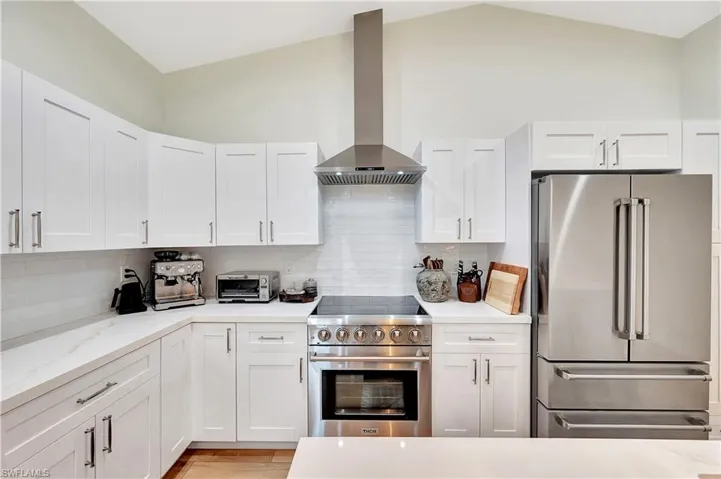 Kitchen featuring wall chimney exhaust hood, vaulted ceiling, white cabinets, and premium appliances