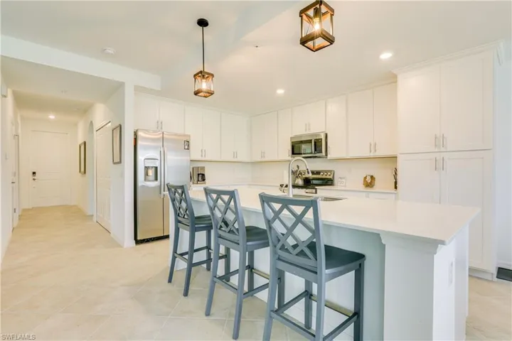 Kitchen with appliances with stainless steel finishes, white cabinets, a breakfast bar area, a kitchen island with sink, and decorative light fixtures