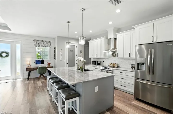 Kitchen featuring stainless steel appliances, a kitchen bar, white cabinets, a center island with sink, and light stone countertops