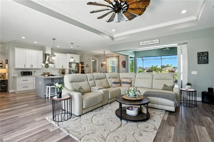 Living room featuring a raised ceiling, recessed lighting, crown molding, light wood finished floors, and ceiling fan