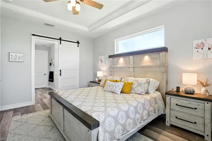 Bedroom featuring a barn door, dark wood-style flooring, ceiling fan, a raised ceiling, and ornamental molding