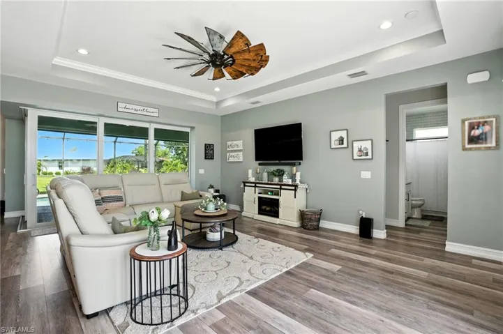 Living area with a tray ceiling, wood finished floors, recessed lighting, ornamental molding, and a fireplace