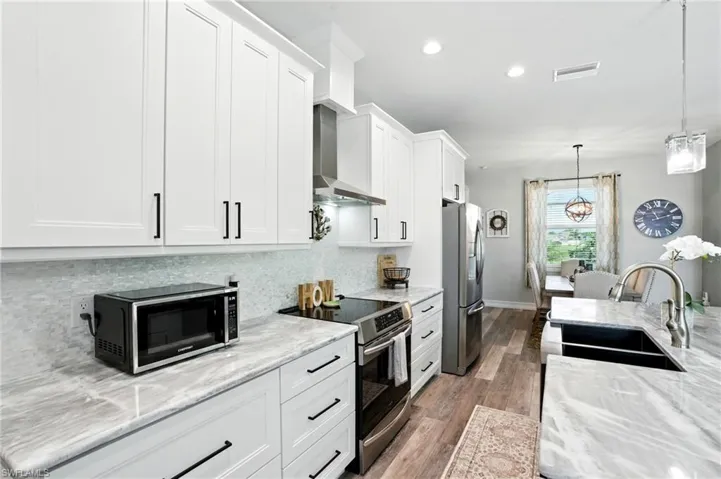Kitchen featuring stainless steel appliances, light stone countertops, pendant lighting, dark wood-style floors, and white cabinets