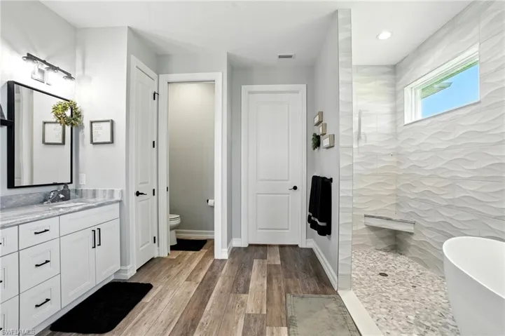 Full bath featuring a walk in shower, vanity, light wood-style flooring, a freestanding bath, and recessed lighting