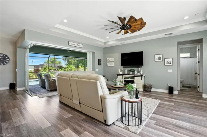 Living area with a raised ceiling, wood finished floors, ceiling fan, recessed lighting, and crown molding