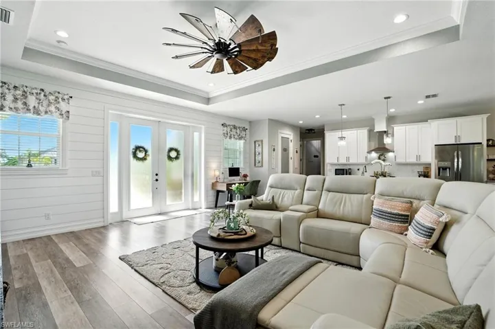 Living area featuring a raised ceiling, french doors, light wood-style flooring, crown molding, and recessed lighting