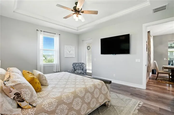 Bedroom with a tray ceiling, wood finished floors, ceiling fan, and ornamental molding