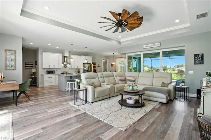 Living area with a tray ceiling, recessed lighting, crown molding, light wood-type flooring, and a ceiling fan