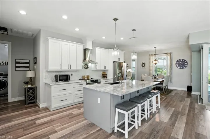 Kitchen featuring a kitchen bar, tasteful backsplash, white cabinets, an island with sink, and light stone counters