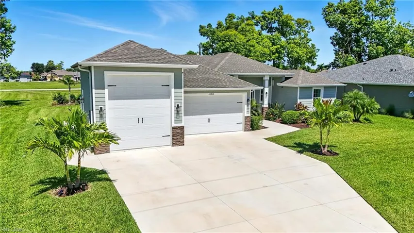 Single story home featuring a front yard, an attached garage, a shingled roof, stone siding, and driveway