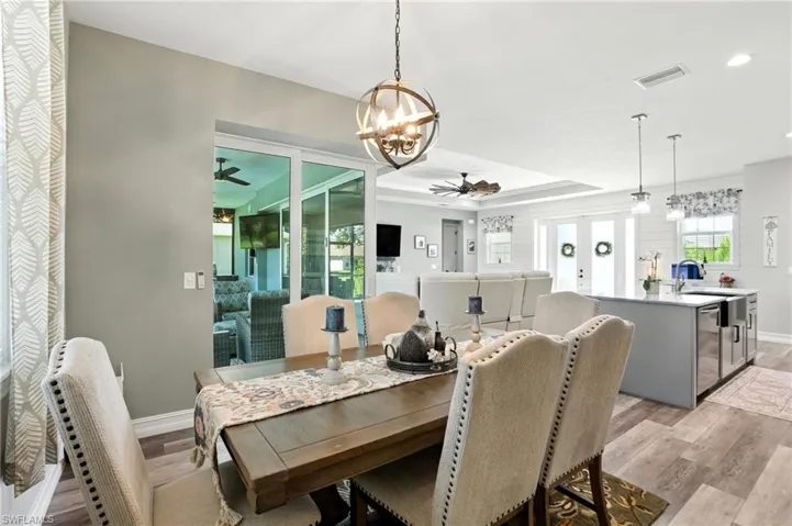 Dining space with a chandelier, a tray ceiling, light wood-type flooring, and ceiling fan