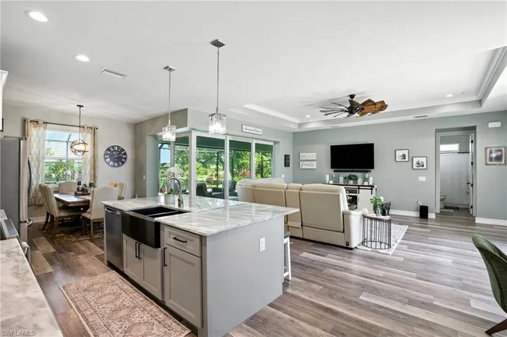 Kitchen with a tray ceiling, light stone countertops, recessed lighting, gray cabinets, and decorative light fixtures