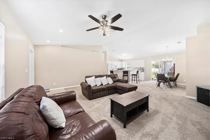 Living area with ceiling fan, carpet flooring, suspended lighting, and lofted ceiling