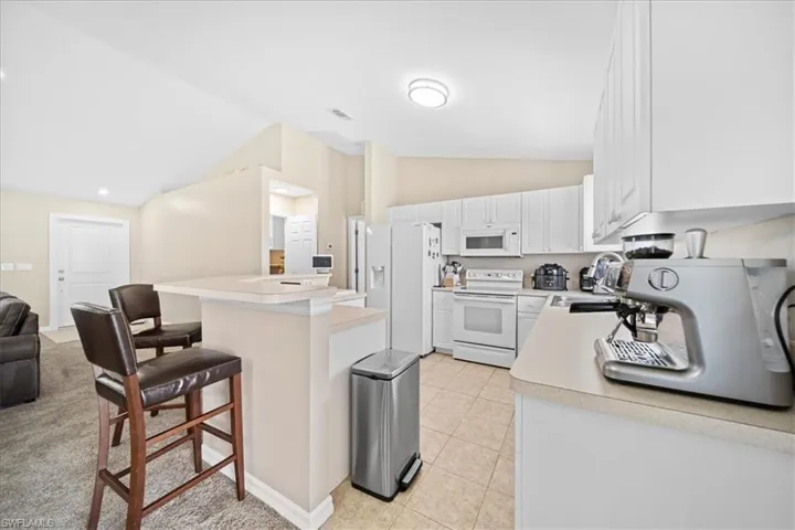 Kitchen with vaulted ceiling, white appliances, light countertops, a breakfast bar, and white cabinetry
