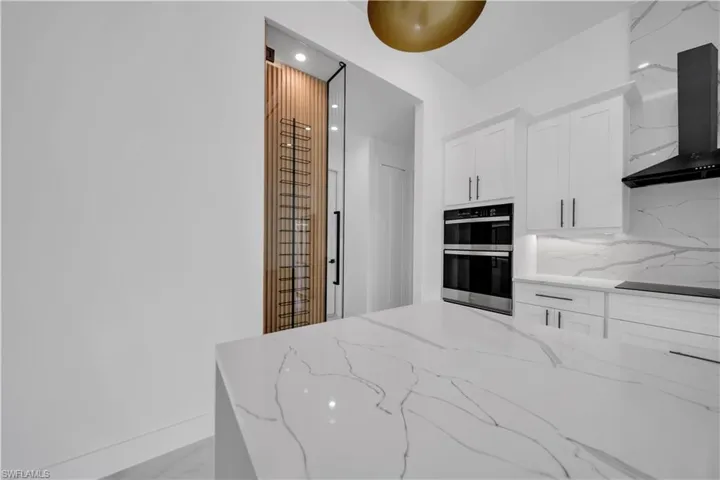 Kitchen featuring light stone counters, white cabinets, stainless steel double oven, recessed lighting, and black electric stovetop