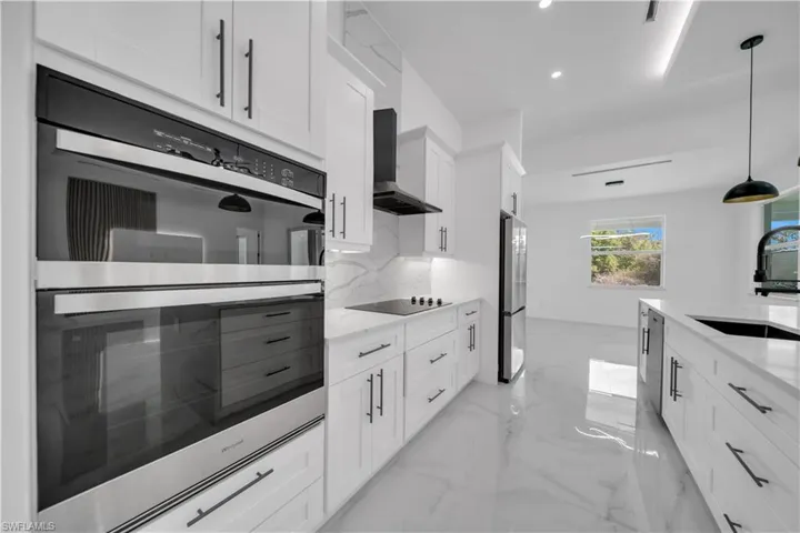 Kitchen featuring stainless steel appliances, white cabinets, light stone countertops, and hanging light fixtures