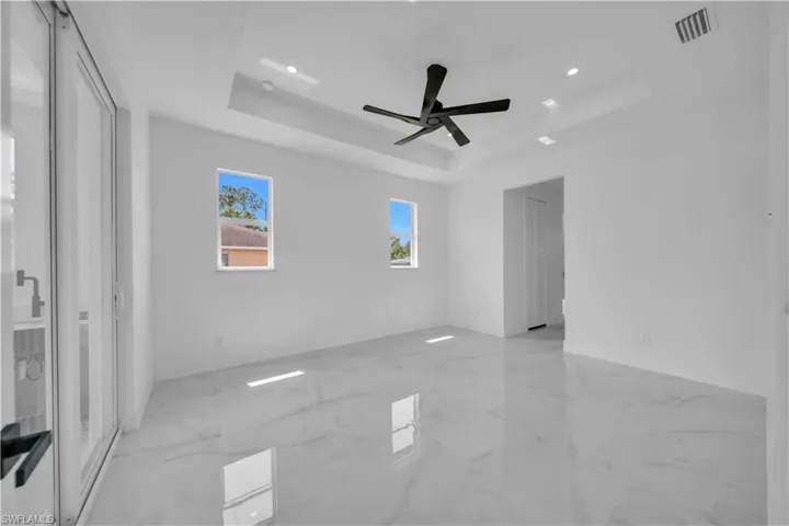 Unfurnished bedroom featuring ceiling fan, a tray ceiling, recessed lighting, and light marble finish flooring