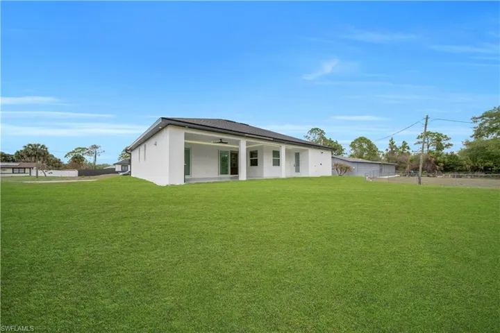 Rear view of house with a yard, stucco siding, ceiling fan, and a patio area