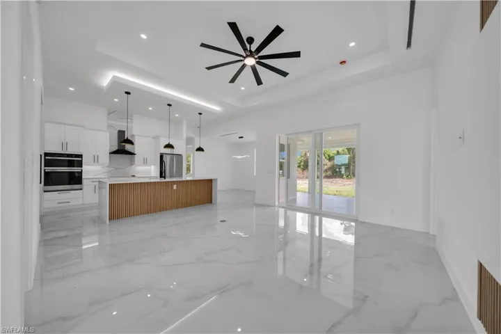 Unfurnished living room with light marble finish floors, recessed lighting, a ceiling fan, and a raised ceiling