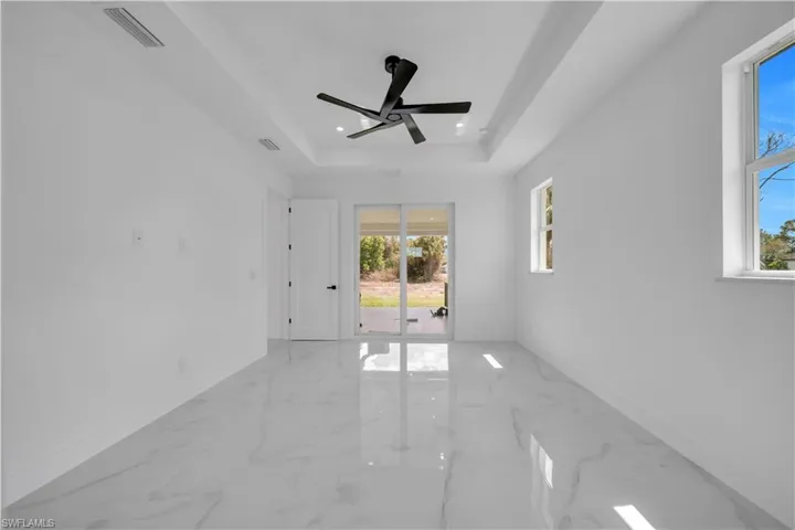 Empty room with ceiling fan, light marble finish flooring, a tray ceiling, and recessed lighting