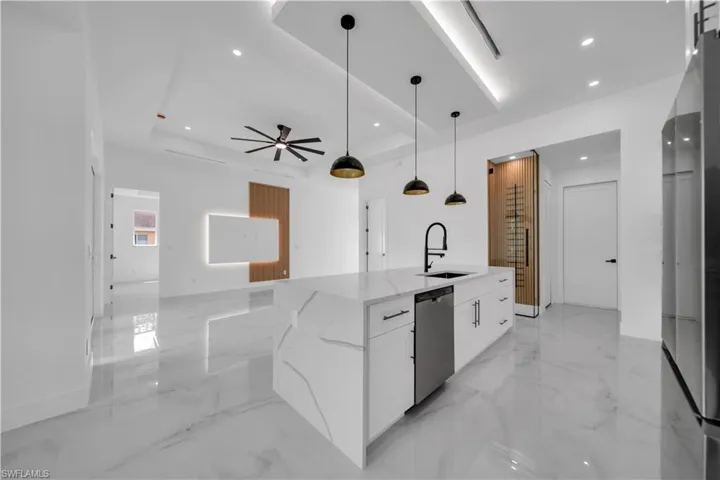 Kitchen with white cabinetry, light stone countertops, light marble finish floors, a kitchen island with sink, and stainless steel appliances