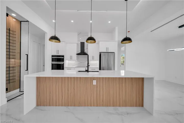 Kitchen with light stone counters, a spacious island, white cabinets, hanging light fixtures, and freestanding refrigerator