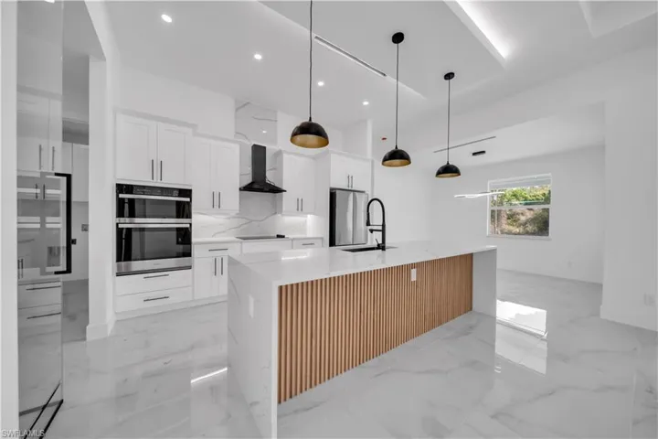 Kitchen with light stone counters, white cabinetry, stainless steel appliances, hanging light fixtures, and a center island with sink