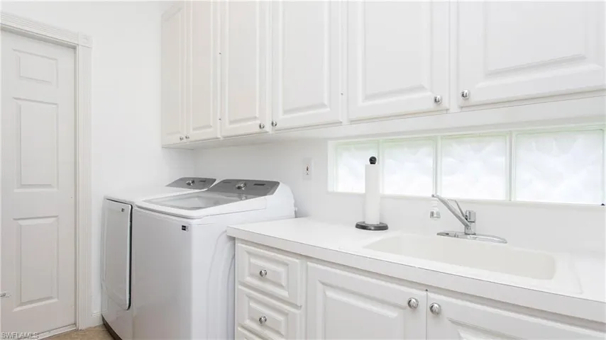 Clothes washing area with washer and clothes dryer, sink, and cabinets