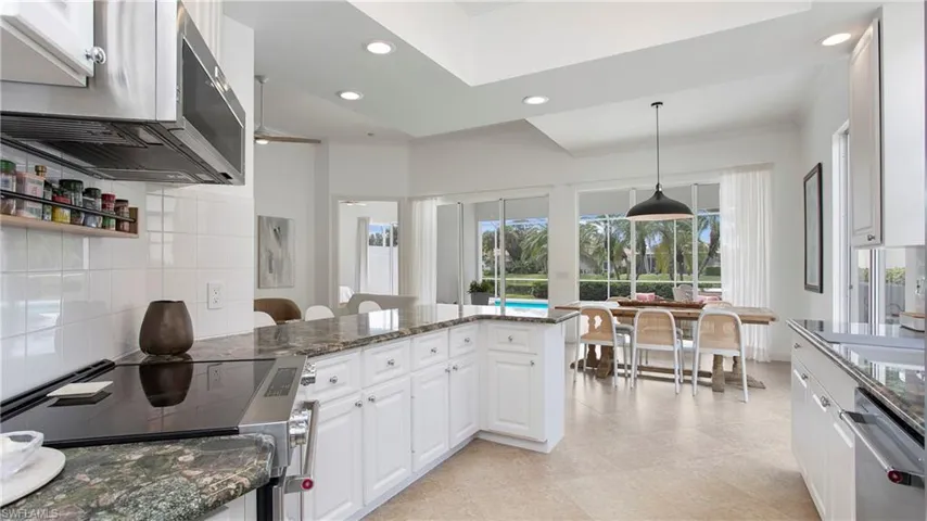 Kitchen with dark stone counters, white cabinetry, stainless steel appliances, and decorative light fixtures