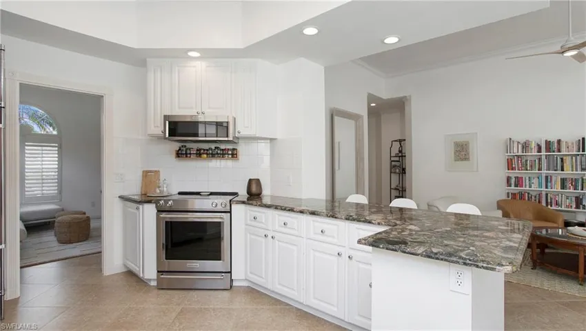 Kitchen with dark stone counters, white cabinets, kitchen peninsula, appliances with stainless steel finishes, and ceiling fan