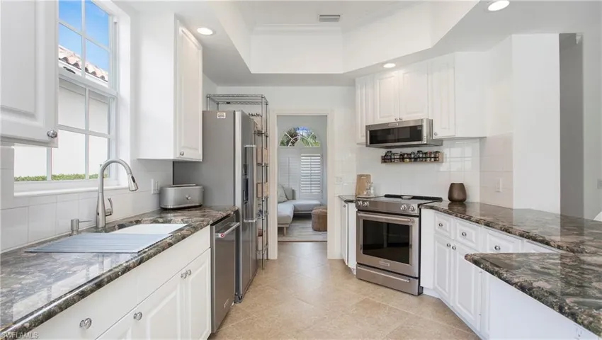 Kitchen with ornamental molding, backsplash, white cabinetry, stainless steel appliances, and dark stone counters