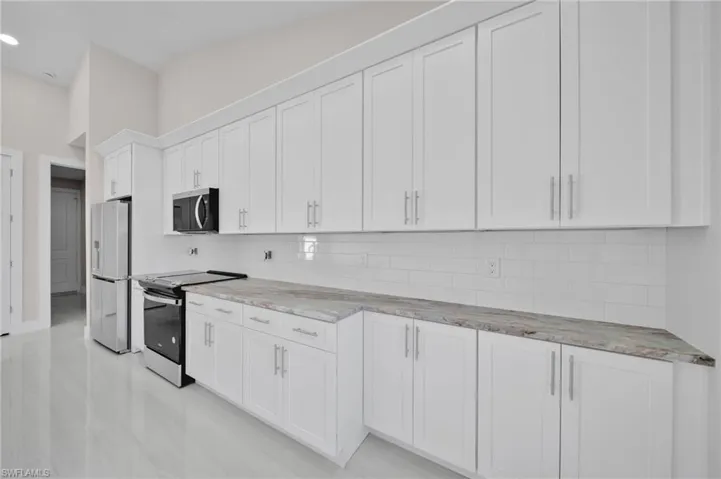 Kitchen featuring recessed lighting, light stone countertops, tasteful backsplash, white cabinetry, and appliances with stainless steel finishes