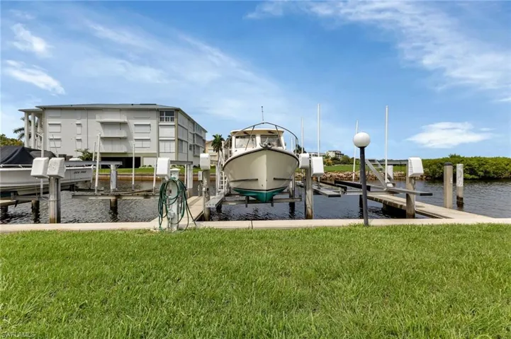 Dock featuring boat lift, a lawn, and a water view