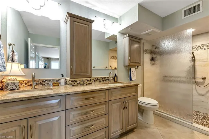 Full bath with a tile shower, double vanity, backsplash, and light tile patterned floors