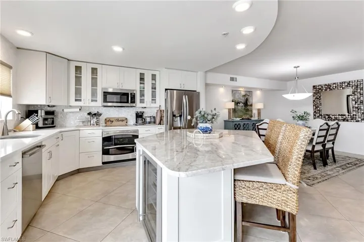 Kitchen featuring white cabinetry, a kitchen bar, stainless steel appliances, light stone counters, and a kitchen island