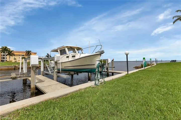 Dock area with boat lift, a water view, and a lawn