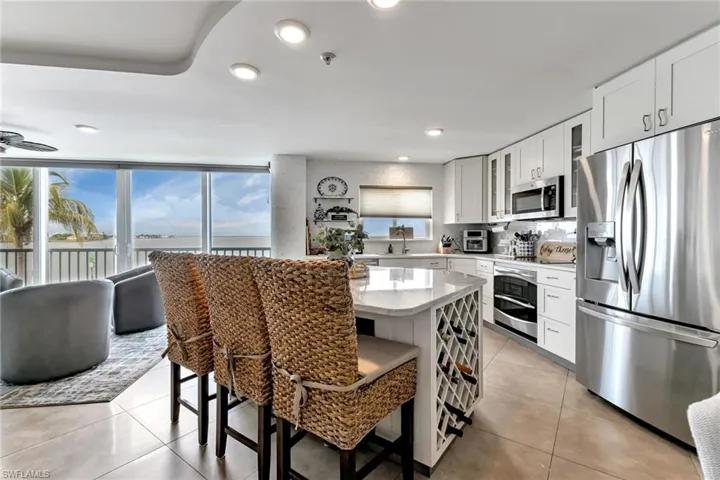 Kitchen featuring stainless steel appliances, glass insert cabinets, light stone counters, a breakfast bar area, and light tile patterned floors