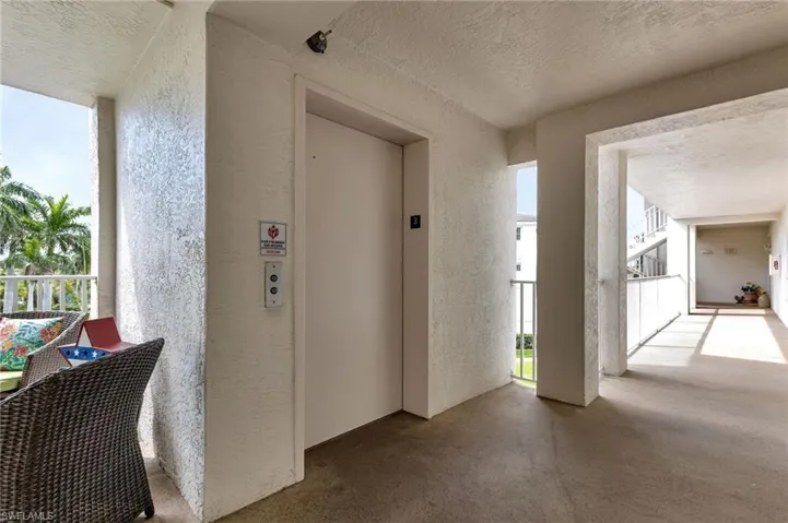 Corridor featuring a textured ceiling, a textured wall, elevator, and concrete flooring