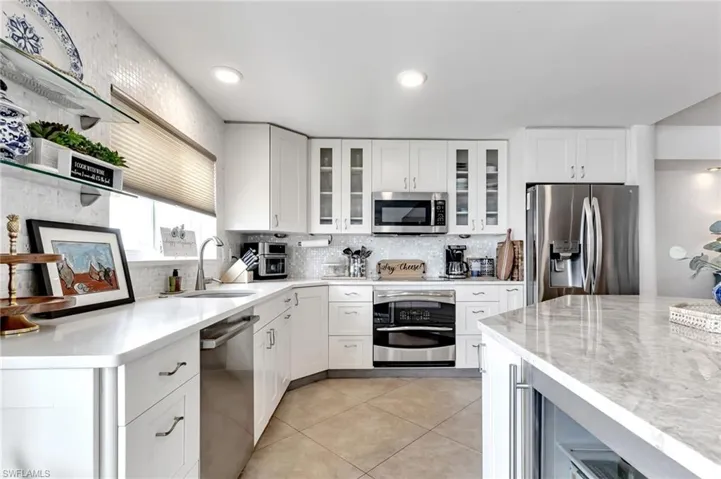 Kitchen featuring light stone countertops, stainless steel appliances, white cabinetry, glass insert cabinets, and recessed lighting
