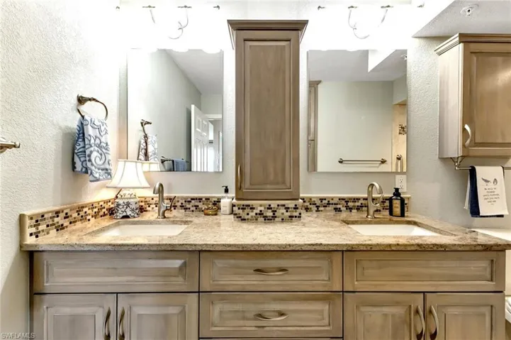 Full bathroom featuring a textured wall, double vanity, and backsplash