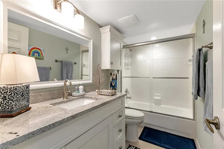 Full bath featuring shower / bath combination with glass door, vanity, and light tile patterned floors