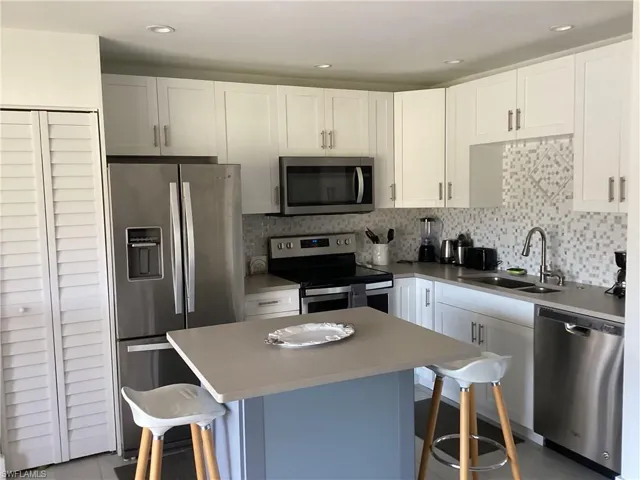 Kitchen featuring sink, stainless steel appliances, a kitchen island, a breakfast bar area, and white cabinets