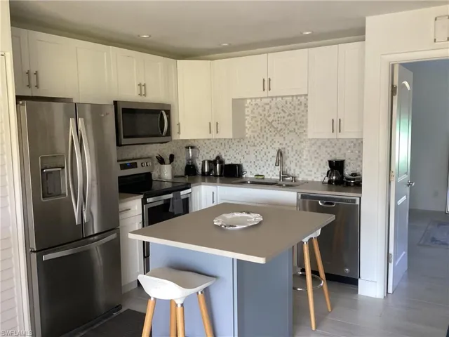 Kitchen featuring decorative backsplash, a breakfast bar, stainless steel appliances, sink, and white cabinetry