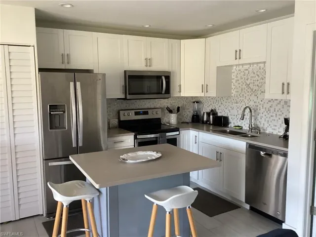 Kitchen featuring a kitchen breakfast bar, sink, appliances with stainless steel finishes, a kitchen island, and white cabinetry