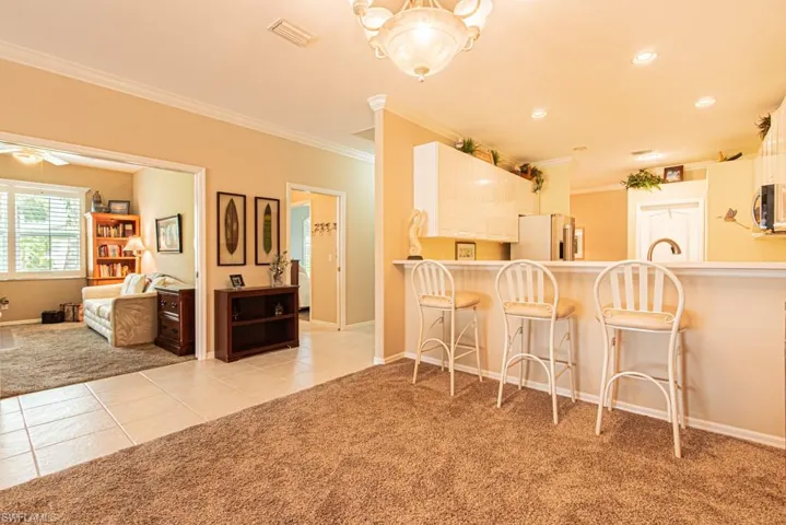 Kitchen with light colored carpet, ornamental molding, light tile patterned floors, a breakfast bar area, and fridge with ice dispenser