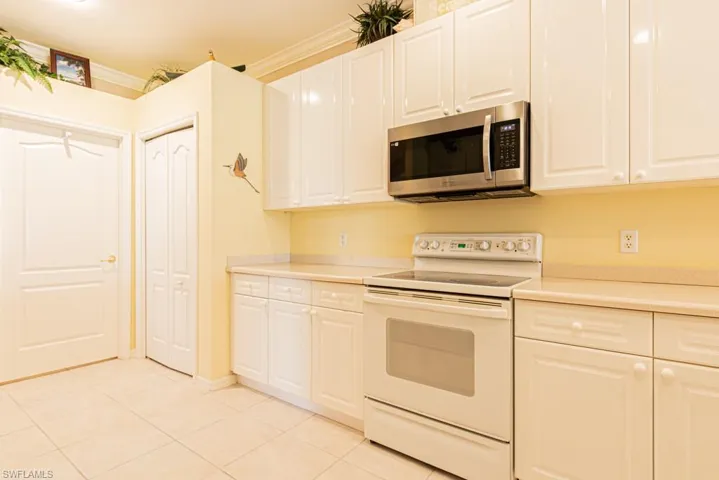 Kitchen with white electric range oven, stainless steel microwave, light countertops, light tile patterned floors, and ornamental molding